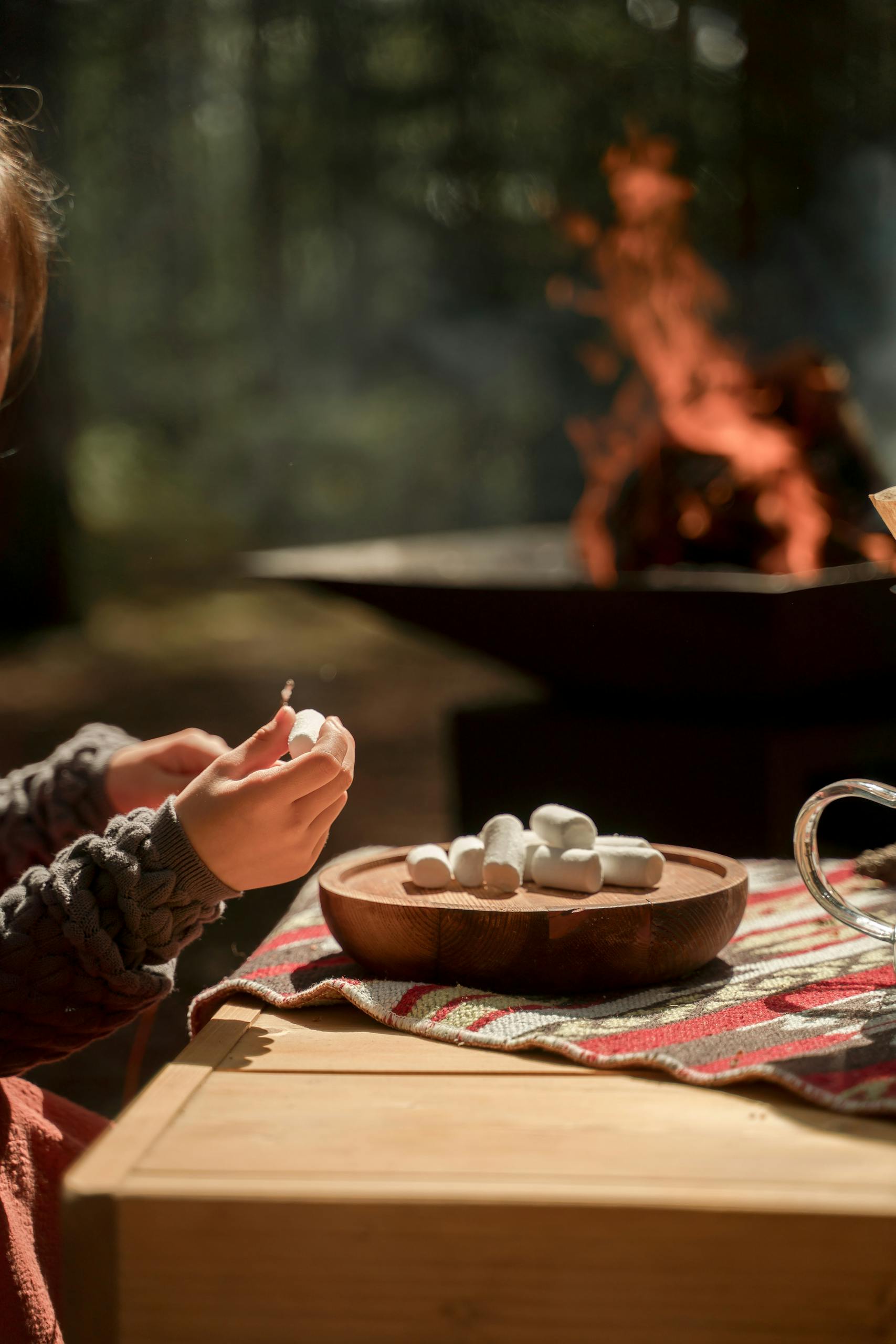 Outdoor setting with a campfire and marshmallows on a table, perfect for camping themes.